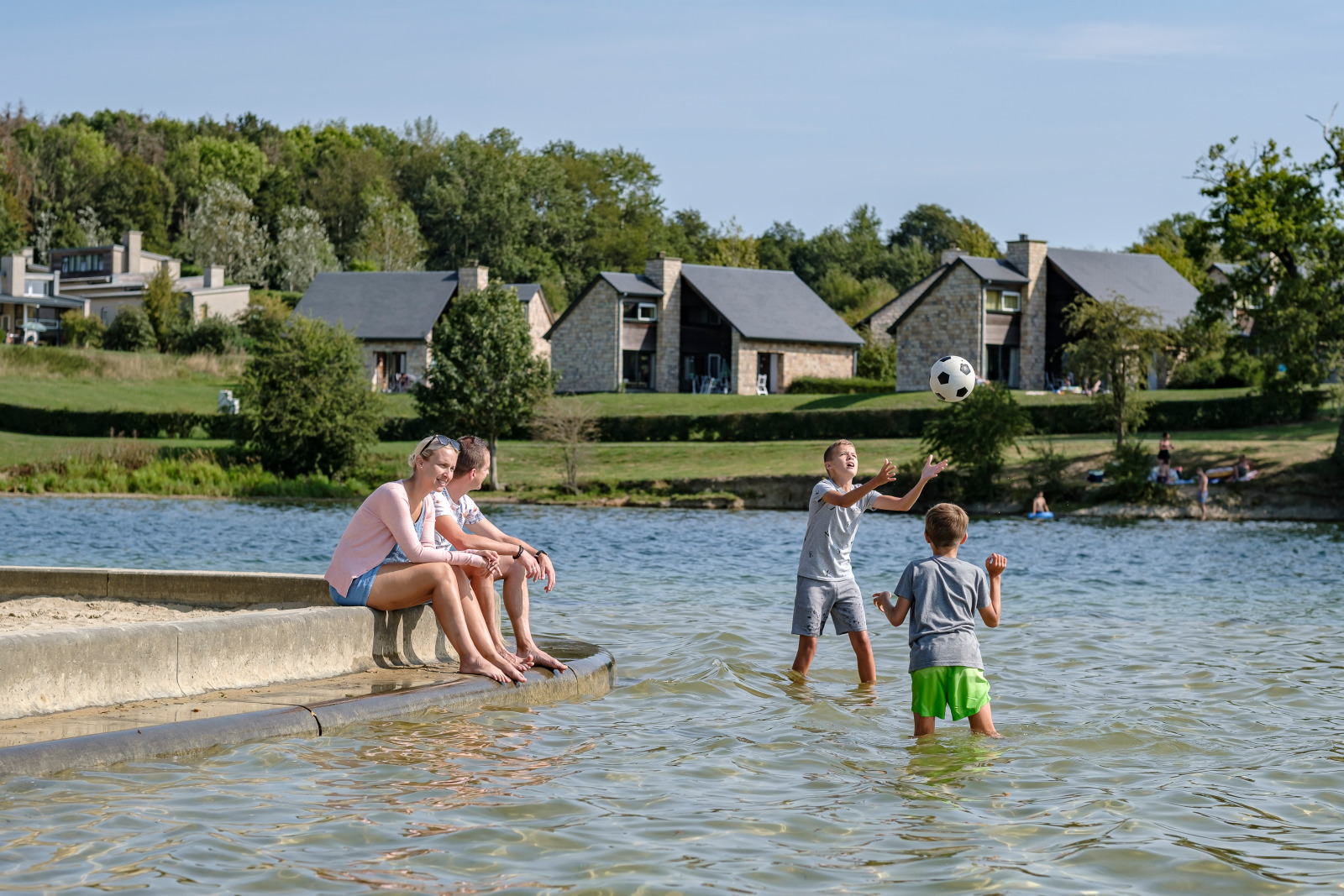 Famille se baignant dans le lac avec en arrière plan le village de vacances