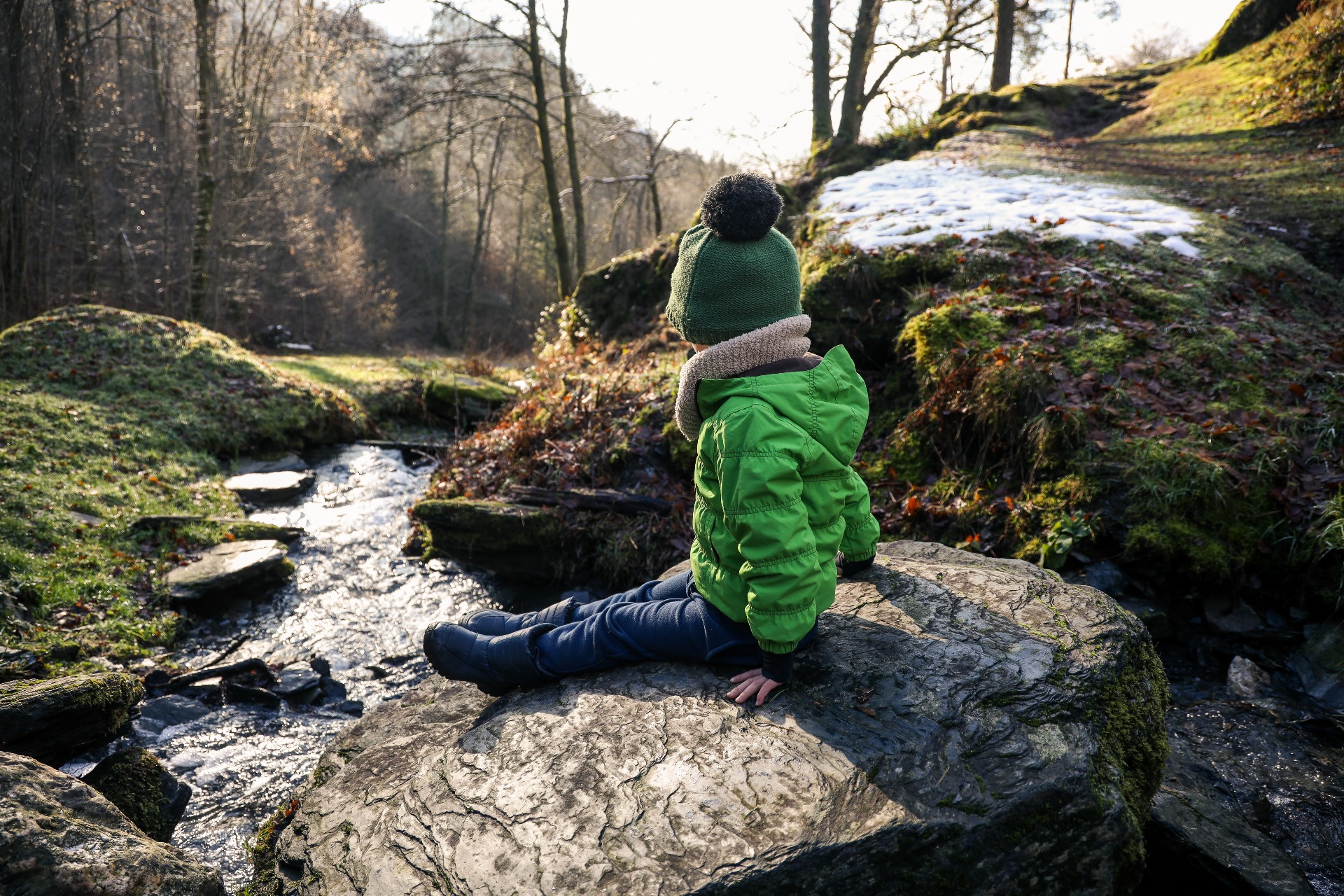 Een kind zit op een rots tegenover een rivier tijdens een winterwandeling