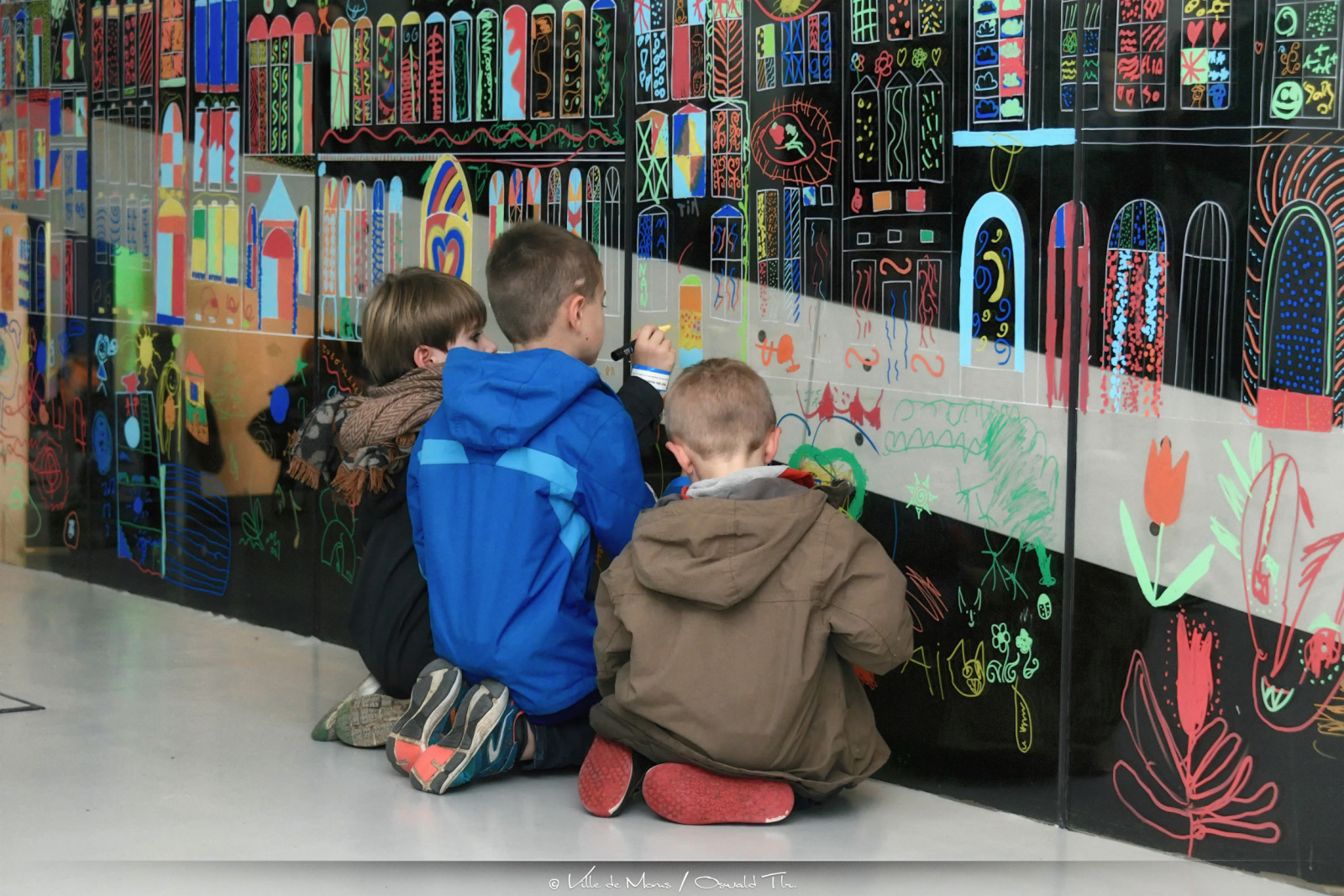 Enfants occupés à dessiner sur un mur en plexiglass