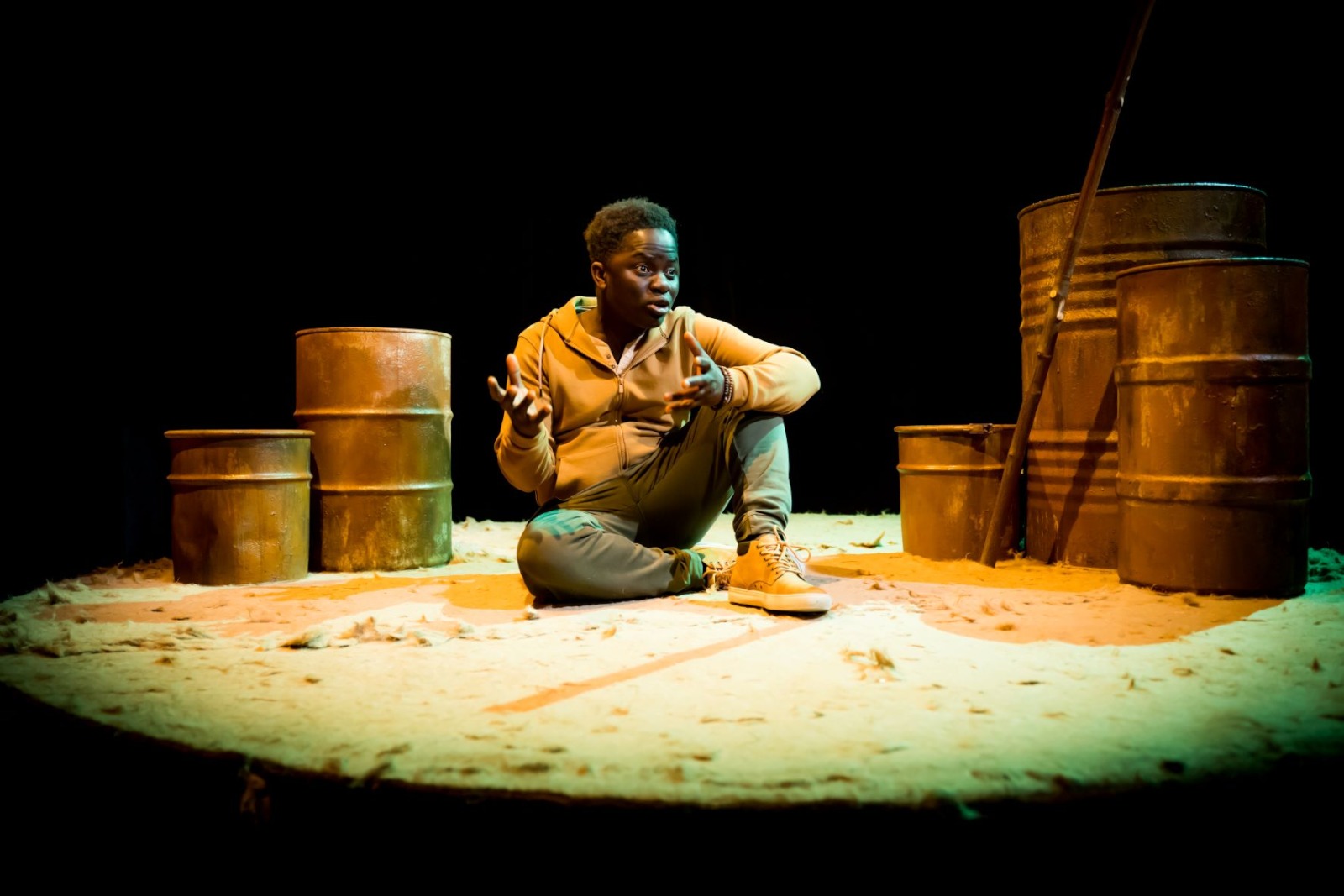 Person seated on stage surrounded by metal barrels