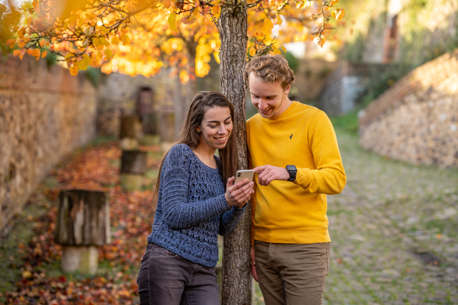 Jeune femme et jeune homme consultant un smartphone dans une rue pavée en automne