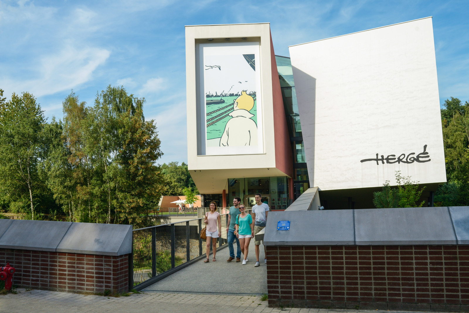 Buitenaanzicht van het gebouw van het Hergé Museum met vier bezoekers die naar buiten komen