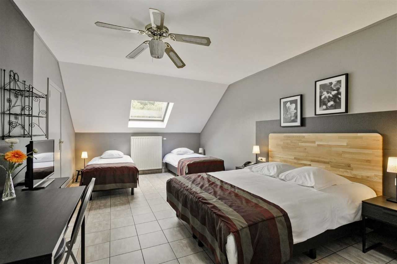 Chambre mansardée composé d'un lit double et de deux lits simples, télévision et ventilateur au plafond