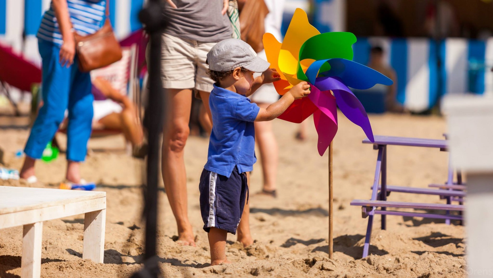 Petit garçon jouant pieds nus dans le sable avec un moulin à vent coloré