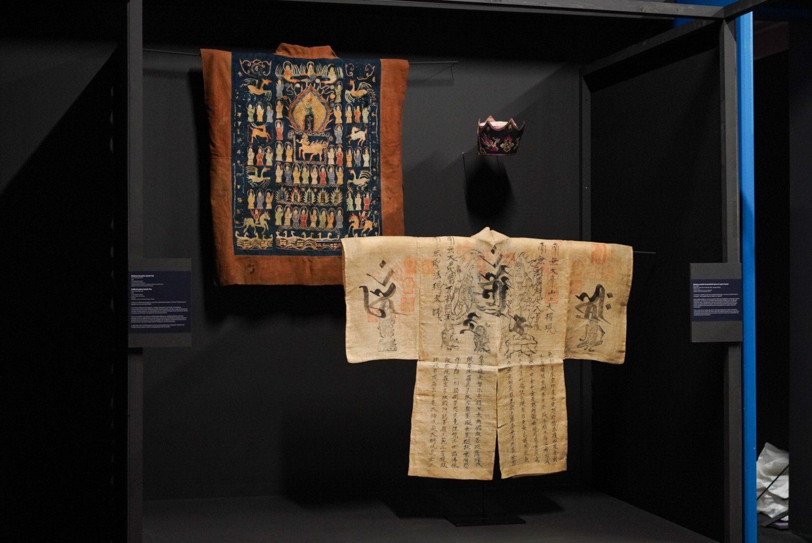 Vitrine exposant un manteau suzukake de yamabushi du Japon, un manteau de prêtre taoïste Yo de Chine du Sud et une coiffe de prêtre taoïste Yao de Chine du Sud