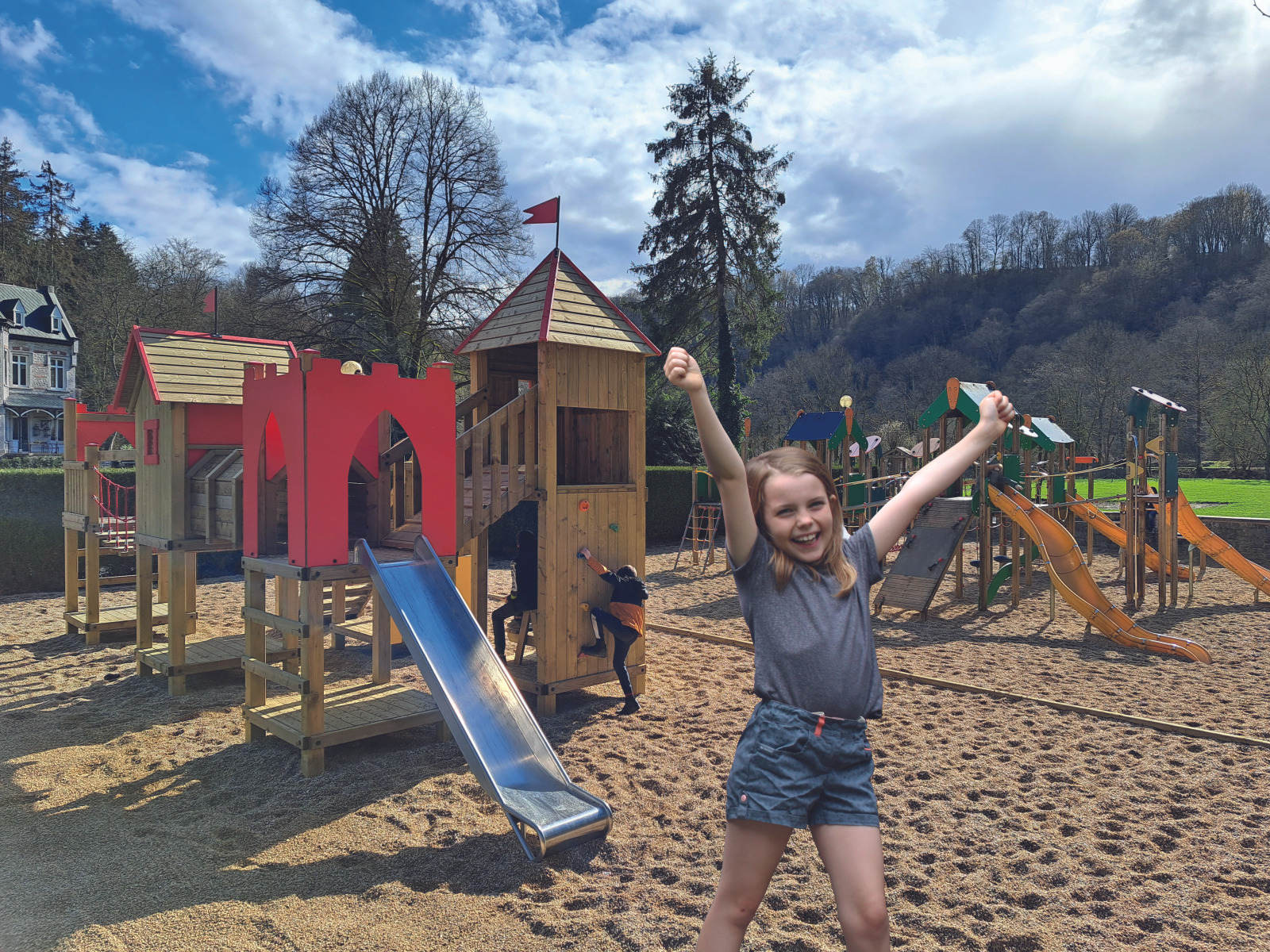 Little girl with a big smile and arms in the air at the Domaine de Palogne playground