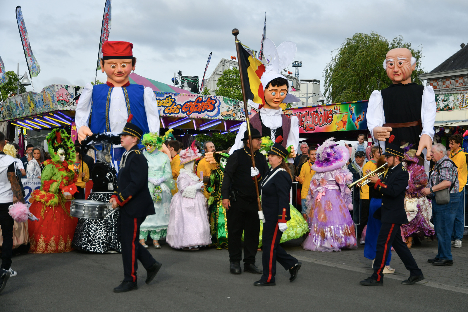 Procession of costumed people and giant puppets following a trumpeter and a drummer