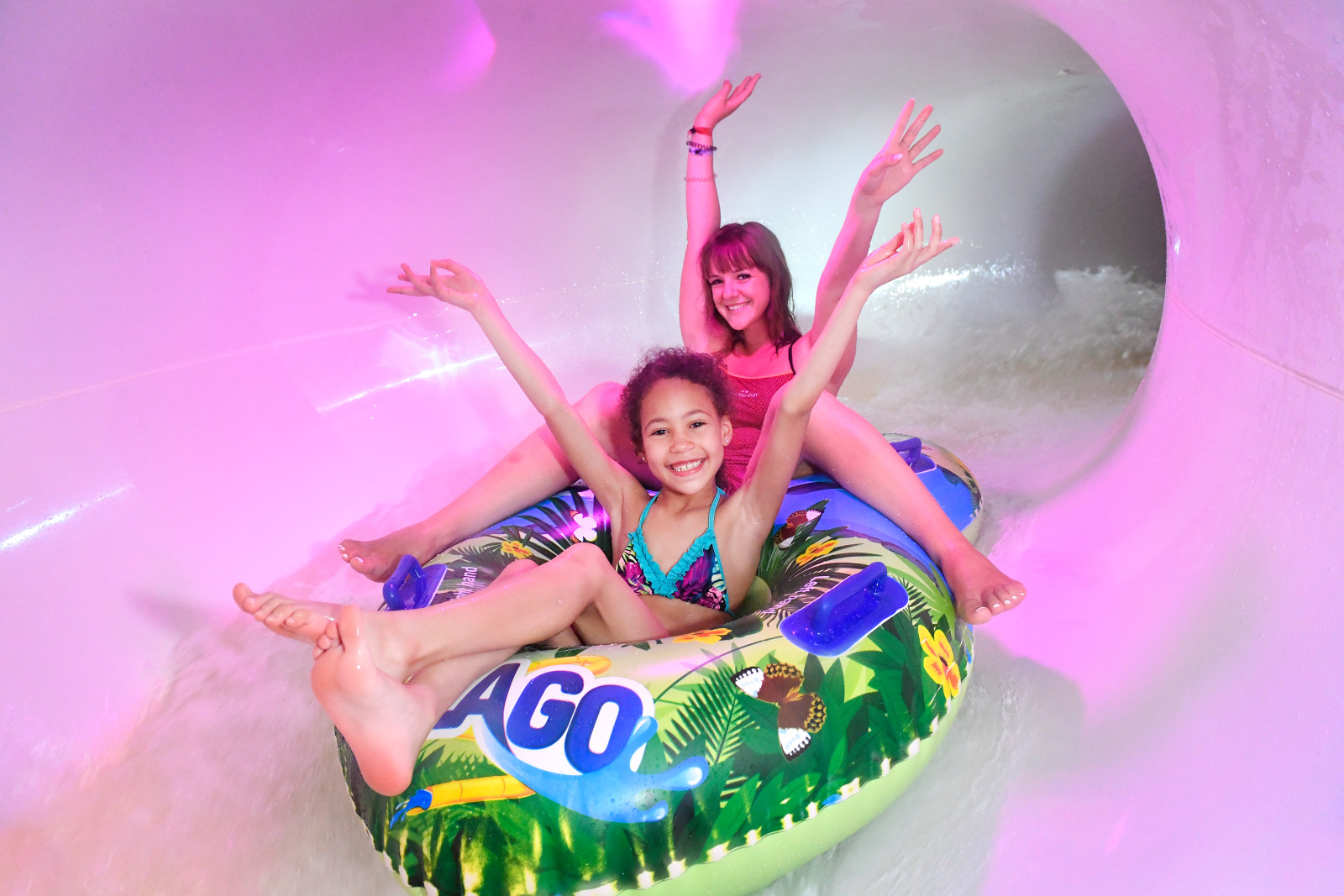 Deux jeunes filles bras levés, assises sur de grosses bouées à l'entrée du toboggan 