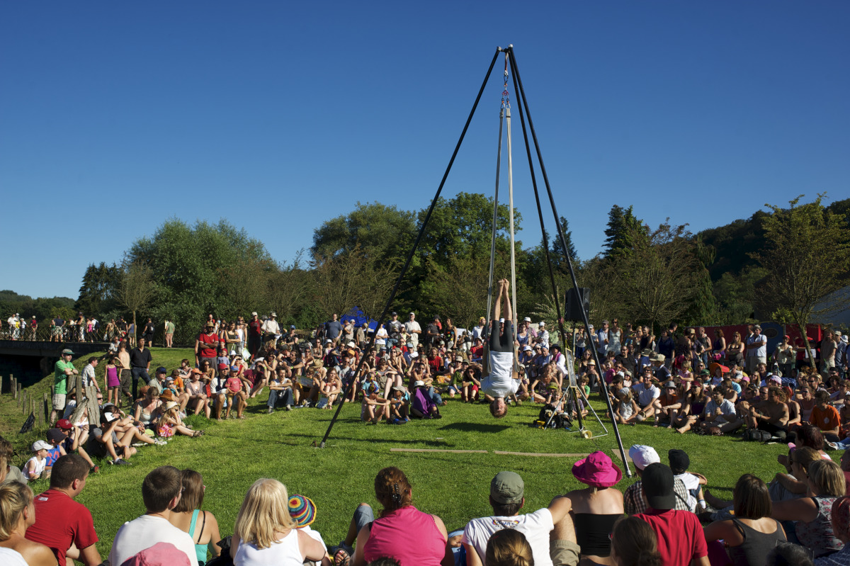 Akrobat, der Kunststücke in der Mitte eines im Gras sitzenden Publikums vorführt.