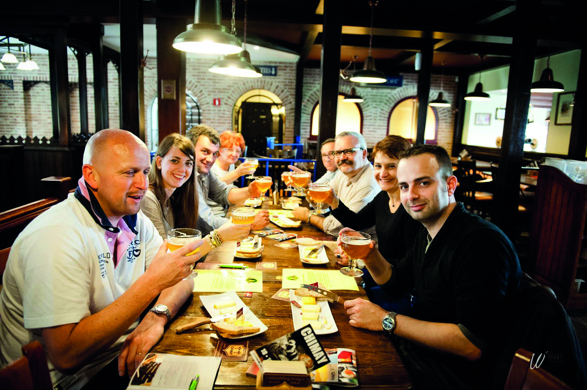 Een groep vrienden proost met Chimay bier tijdens een maaltijd in restaurant Auberge de Poteaupré.