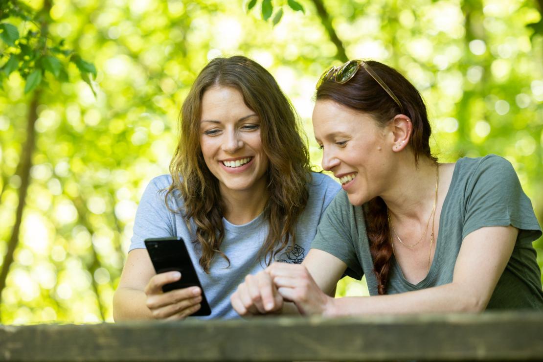 Deux filles assises dans un parc consultent un smartphone