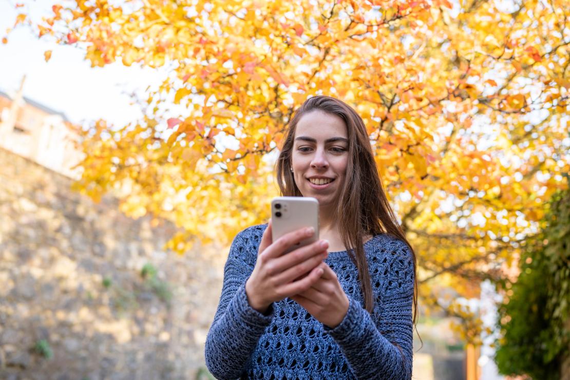 Une femme consulte en automne la web app du Pass sur son smartphone