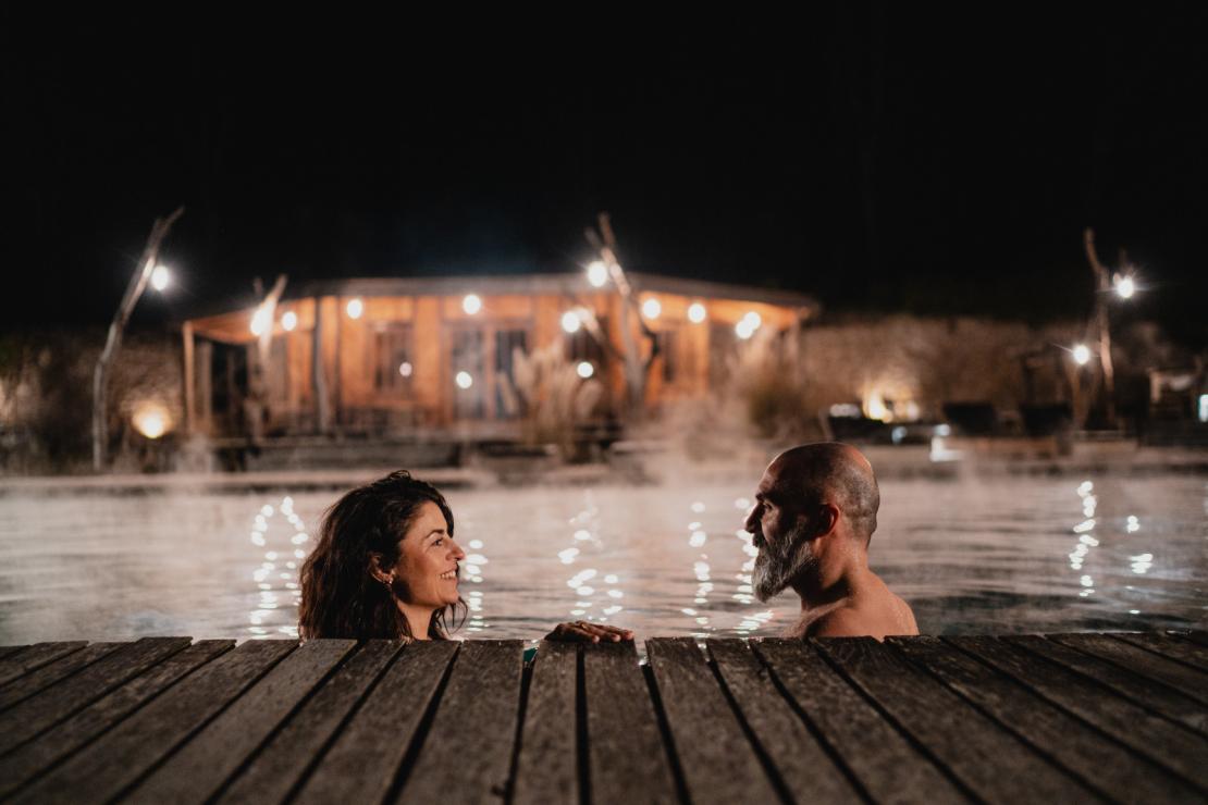 Un couple se baigne de nuit dans la piscine extérieure du Domaine de Ronchinne en hiver