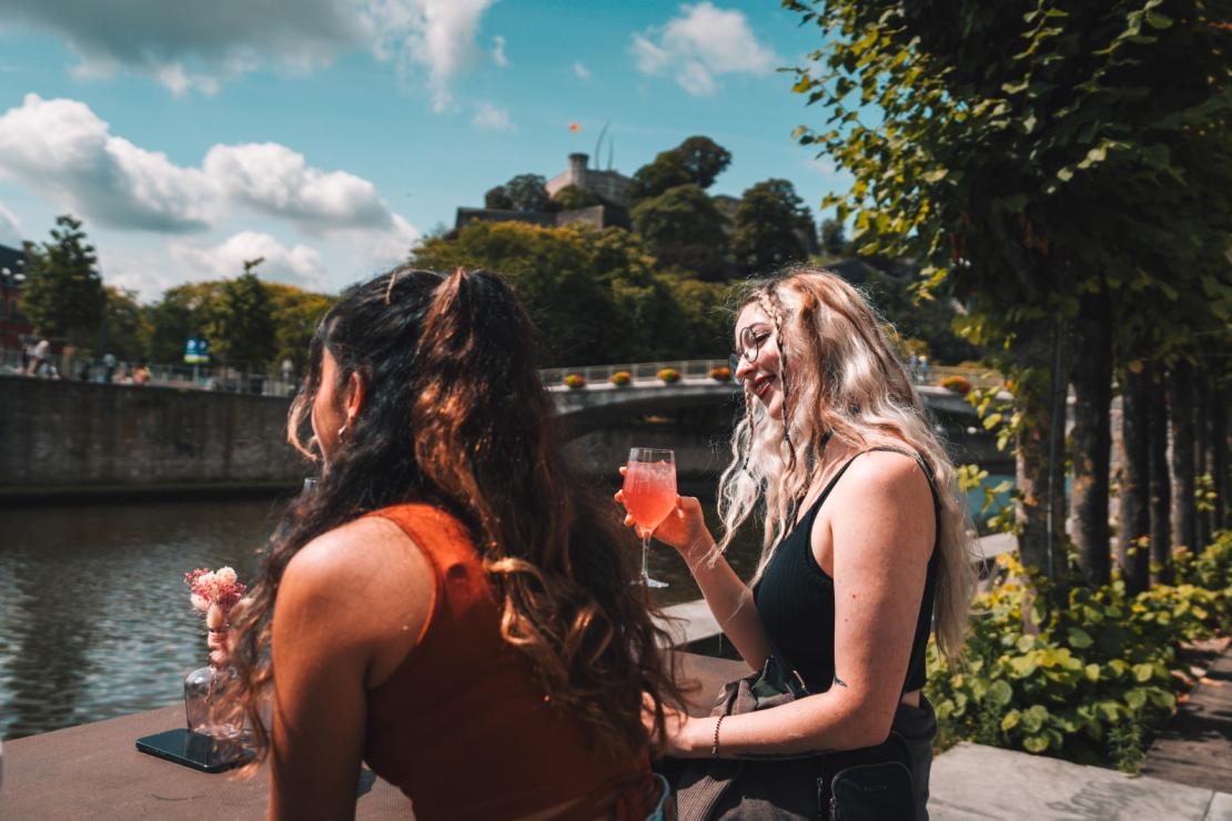 2 jeunes femmes boivent un verre sur les quais de Namur avec la citadelle en arrière-plan