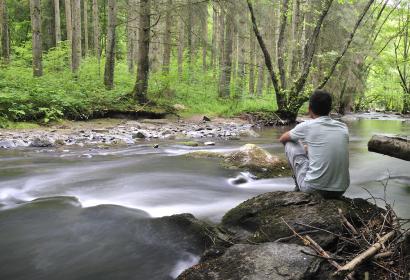 Man sitting on a rock and looking at the Lesse river, in Ardenne, Belgium