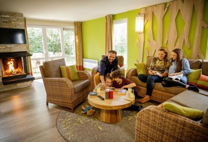 Famille installée dans le salon avec cheminée d'un chalet du village de vacances Center Parcs Les Ardennes