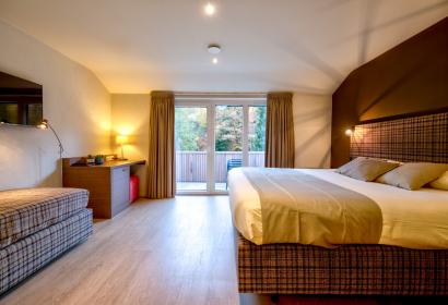 Doppelbett, Tisch und Terrassentür eines Zimmers im Hotel Val d'Arimont