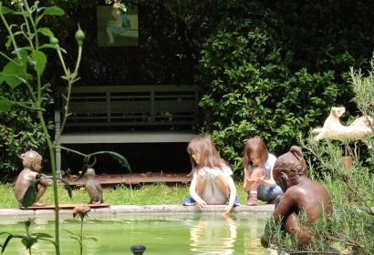 Girls playing on the edge of a pool, next to bronze statues