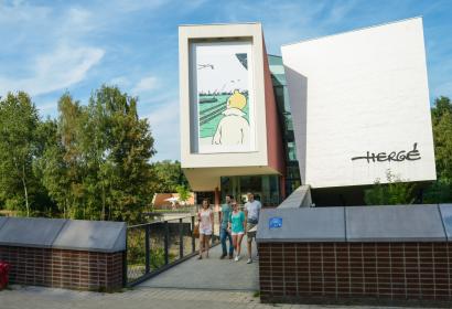 Buitenaanzicht van het gebouw van het Hergé Museum met vier bezoekers die naar buiten komen