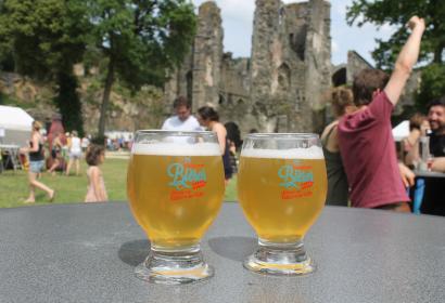 Zwei Biergläser auf einem Tisch mit der Abtei von Villers-la-Ville im Hintergrund