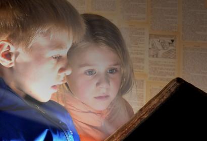 Photo of 2 children reading, captivated, an old grimoire