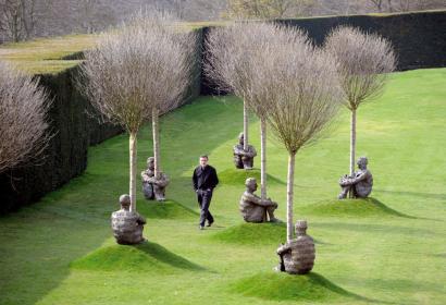 Foto des Künstlers und seiner in die Vegetation eines Gartens eingebetteten Skulpturen