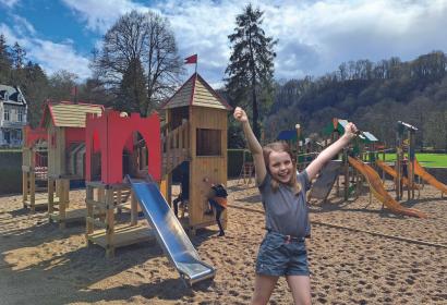 Little girl with a big smile and arms in the air at the Domaine de Palogne playground