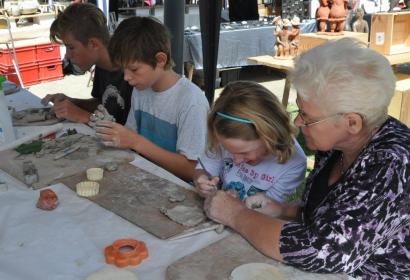 Children practicing pottery under the watchful eye of their grandmother