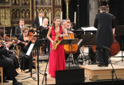 Saxophoniste en robe rouge entourée d'un orchestre dans l'enceinte de la Collégiale de Dinant