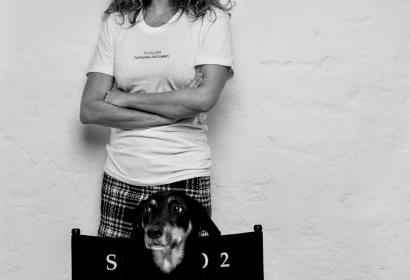 Portrait de Julie Ferrier placée derrière une chaise de metteur en scène sur laquelle est assis un chien