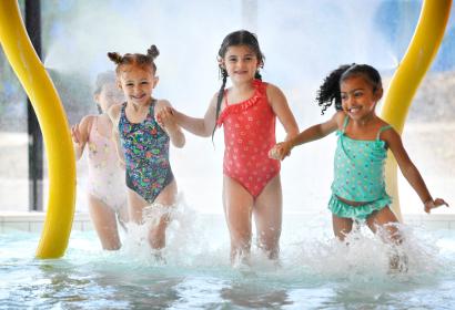 4 petites filles qui, main dans la main, courent dans l'eau en direction du photographe