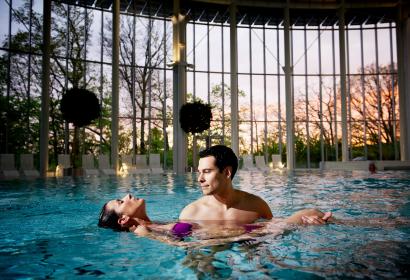 Man carrying his partner into a swimming pool so that she can float on the surface of the water