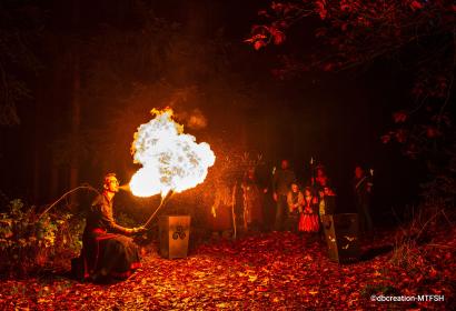 Man spitting fire in the forest in front of spectators wearing masks and disguises