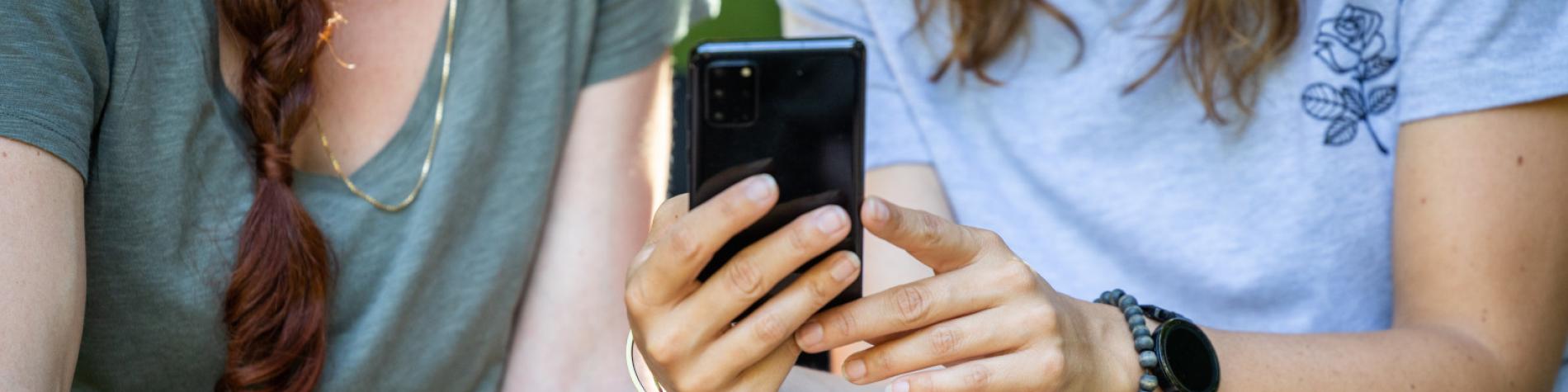 Zwei Mädchen rufen gemeinsam die Informationen ab, die auf dem Bildschirm eines Smartphones angezeigt werden.