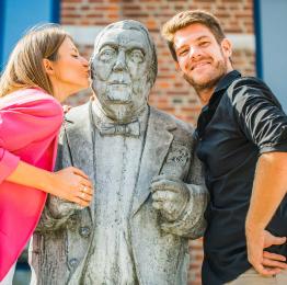 Photo d'un couple se tenant à côté de la statue de Raymond Devos à Rochefort