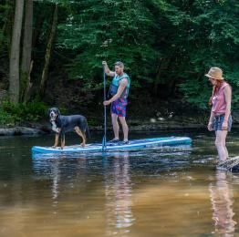Un homme avec son chien sur un paddle et 2 jeunes filles qui les regardent passer