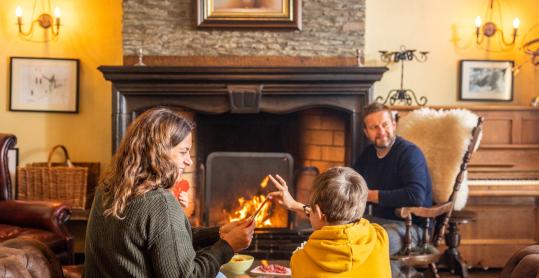 In a lodge, a family plays cards and has an aperitif by the lit fireplace