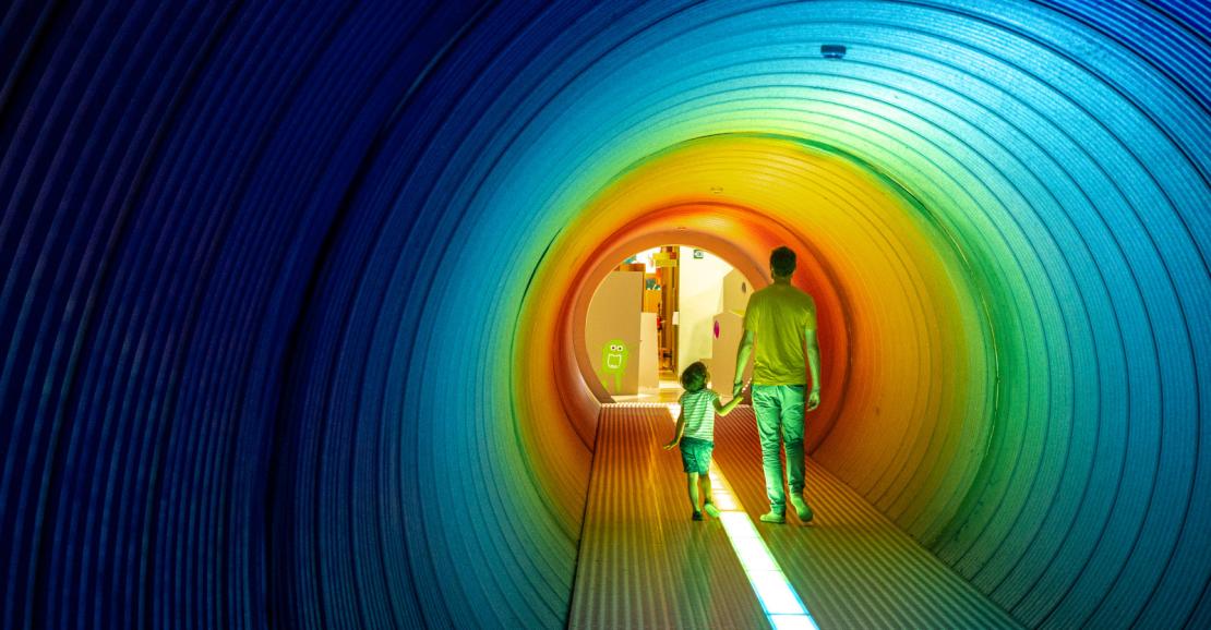 Un père et son fils sont dans le couloir coloré qui mène au musée scientifique Sparkoh