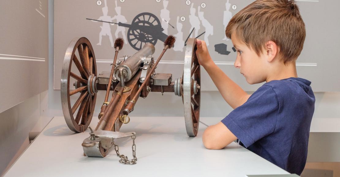 Enfant à l'intérieur du musée, regardant une maquette de canon